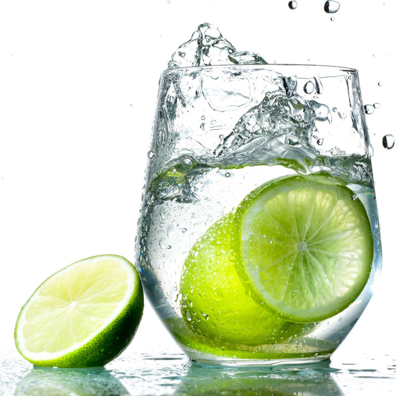 A glass of Lime Hard Seltzer with fresh limes next to it.